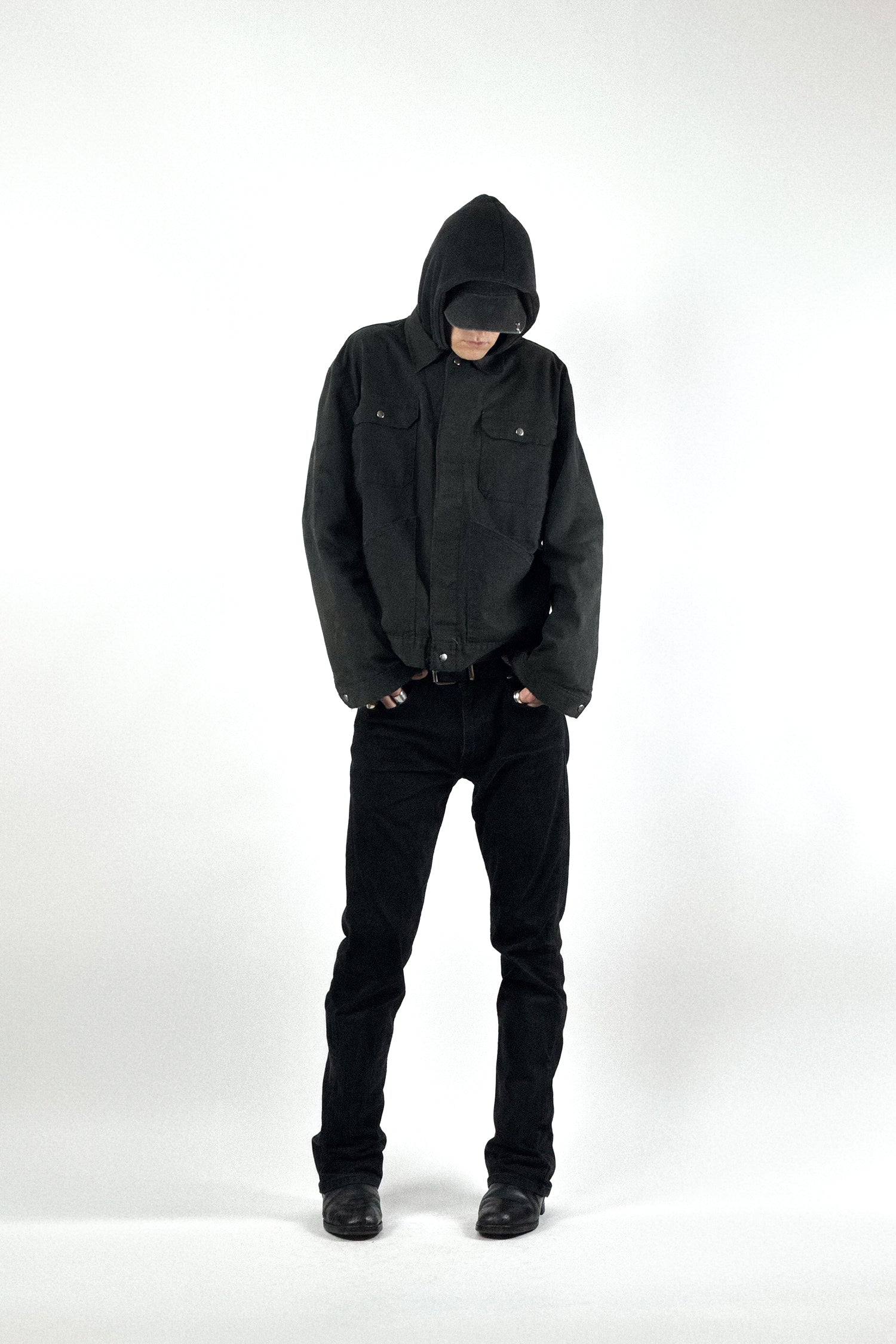 Künstlerisches All-Black-Outfit bestehend aus einer schwarzen Vintage Workwear Jacke, Kapuzenpullover, schwarzer Jeans und Biker Lederboots.