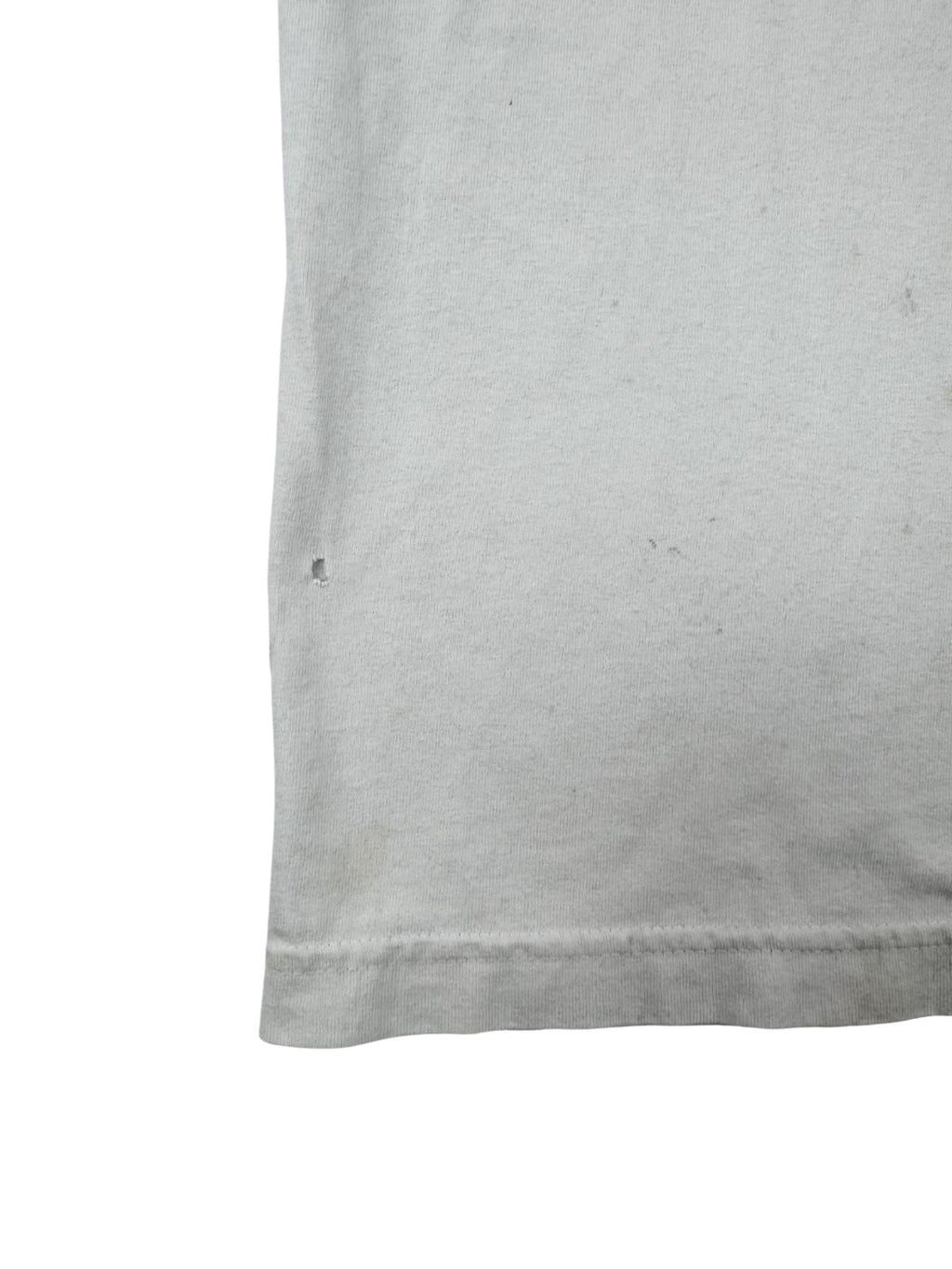 Makro-Ansicht eines kleinen Lochs im weißen Stoff des Vintage-Shirts, ein typisches Merkmal für getragene „Distressed“ Second-Hand-Kleidung.