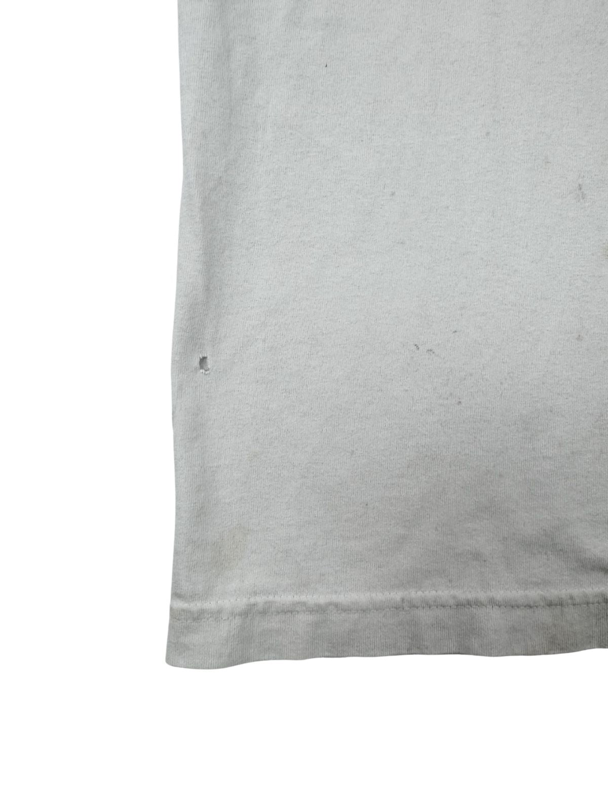 Makro-Ansicht eines kleinen Lochs im weißen Stoff des Vintage-Shirts, ein typisches Merkmal für getragene „Distressed“ Second-Hand-Kleidung.